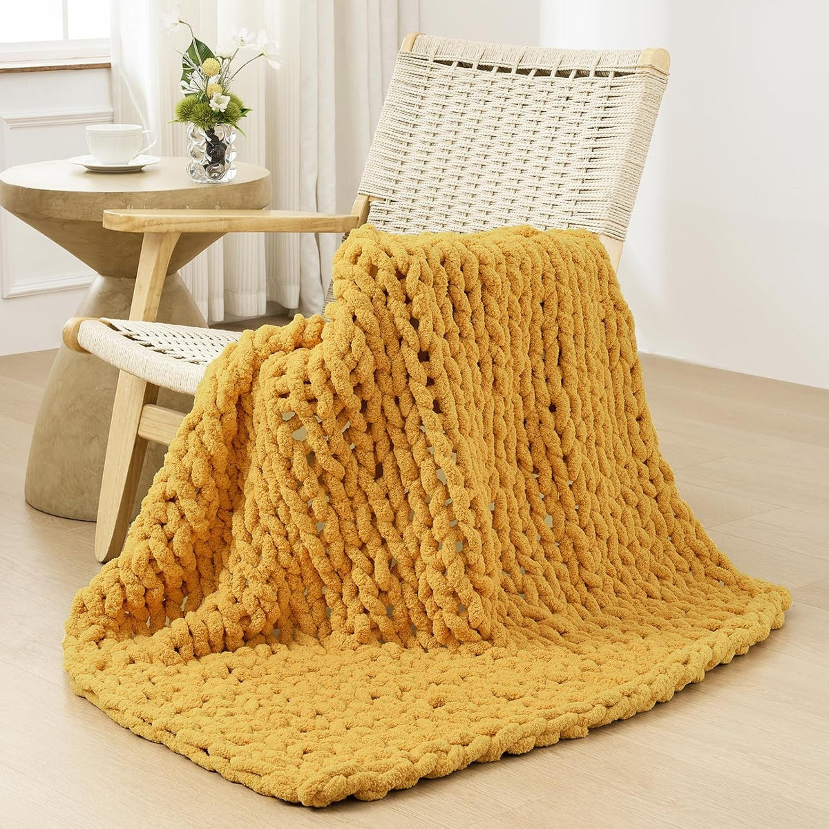 Chunky mustard-yellow knit throw draped over a woven lounge chair and spilling onto the floor
