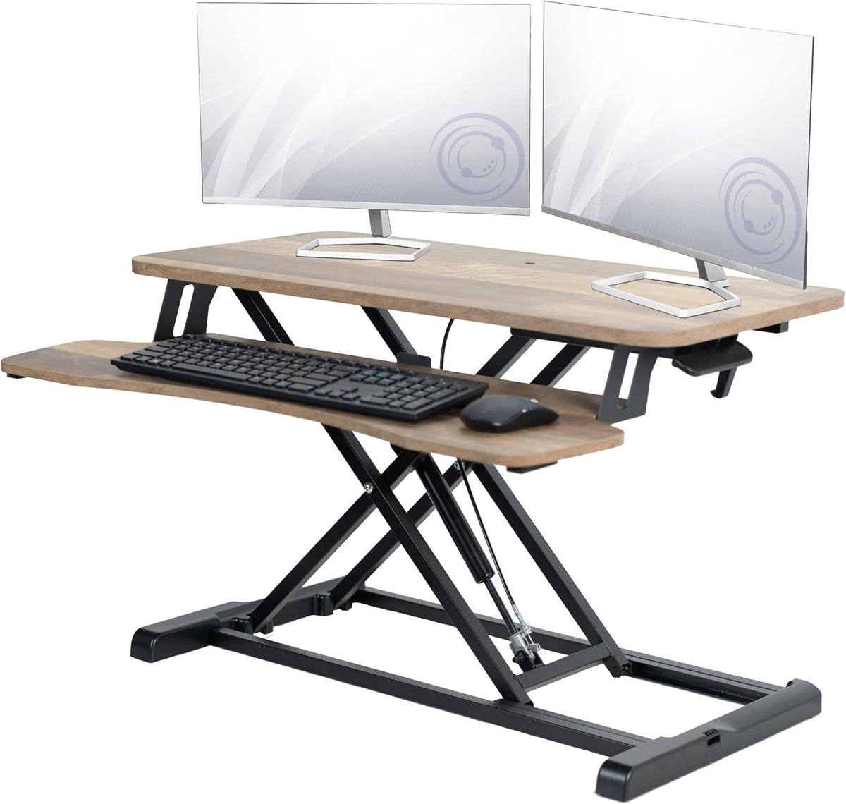 Angled view of a brown wood-finish standing desk converter holding a keyboard and two monitors.