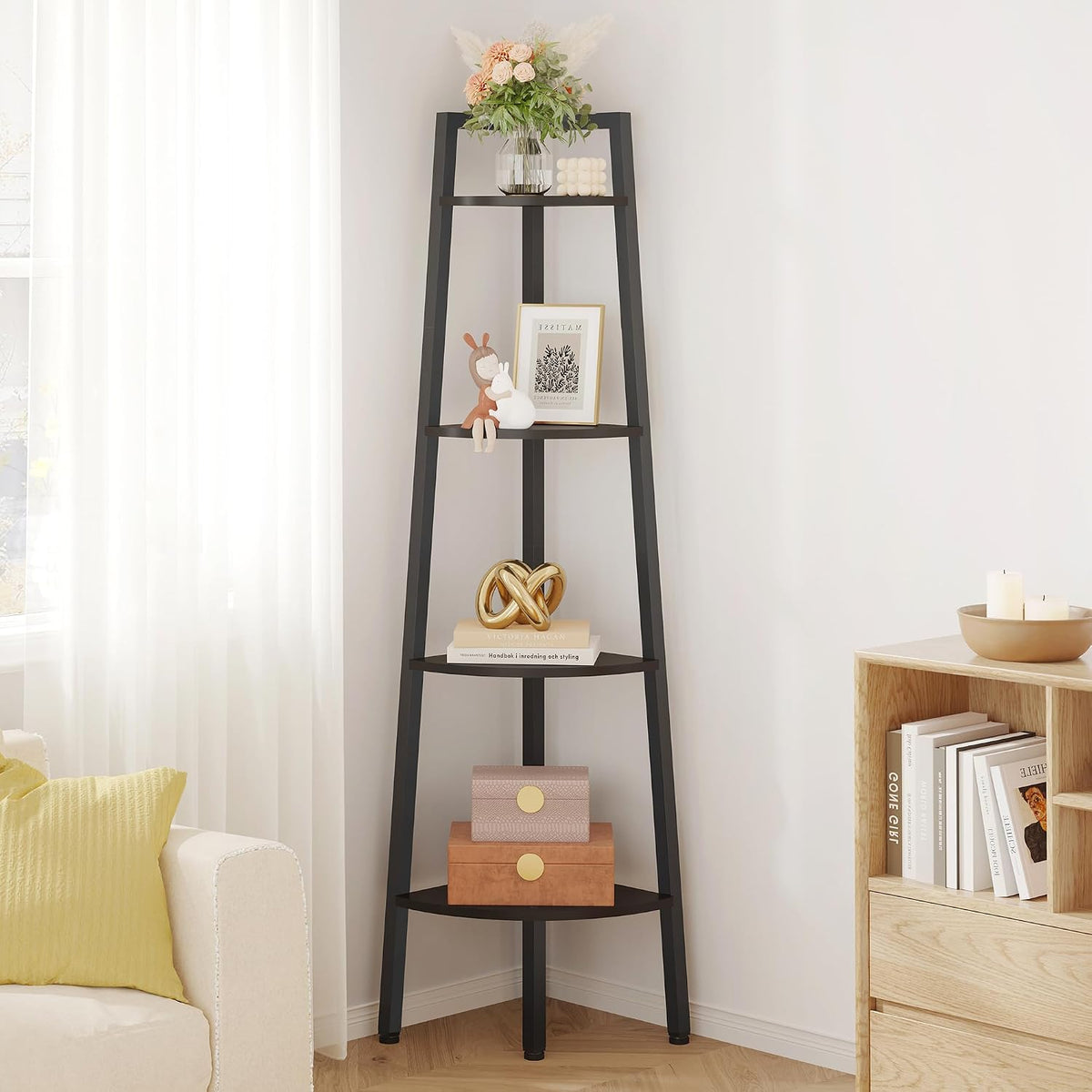 Angled corner view of the black ladder shelf with floral vase on top and stacked decorative boxes below.