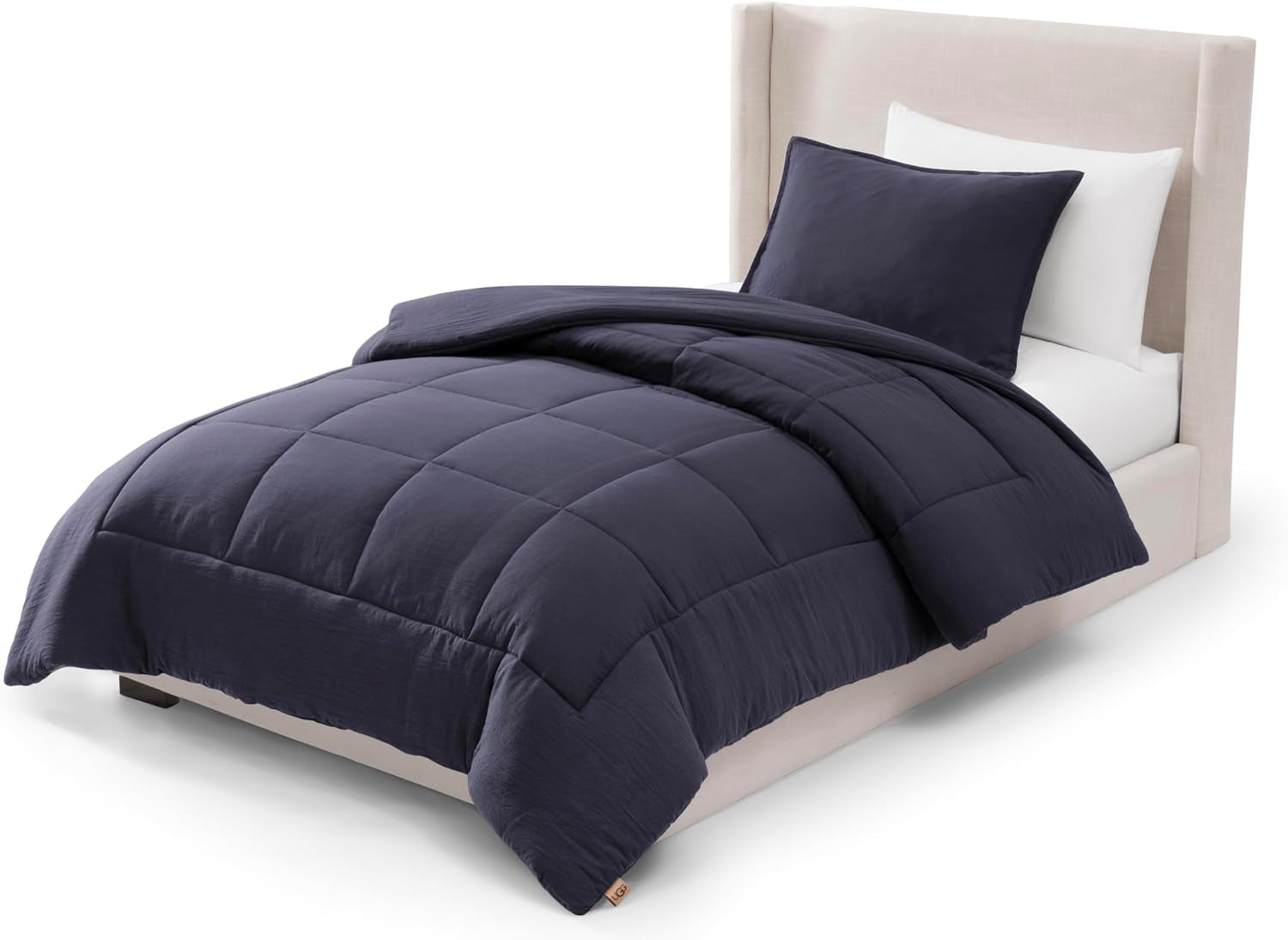 Angled view of a single bed dressed in a deep navy box‑stitched comforter and matching shams.