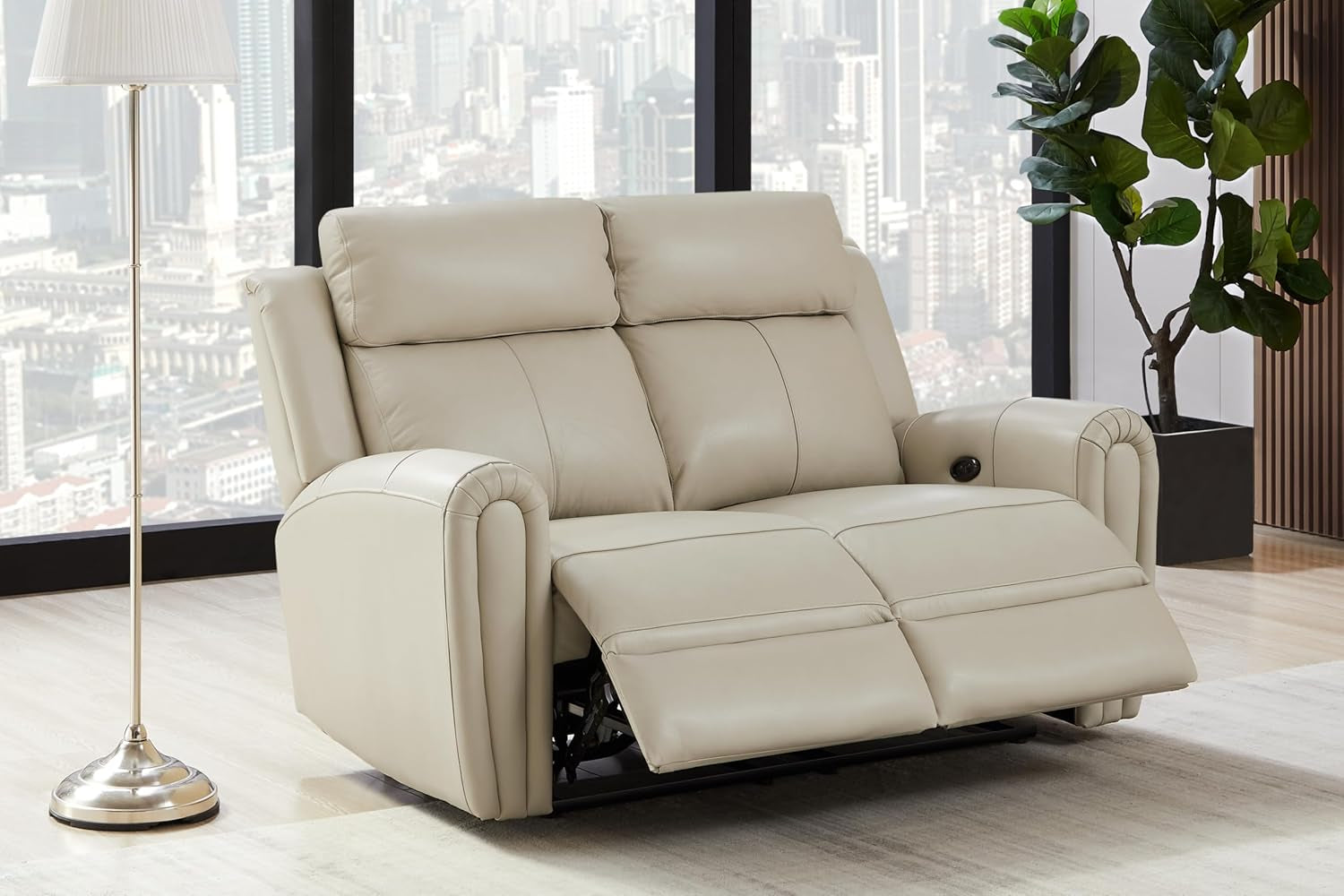 Cream leather power reclining loveseat shown with footrests extended next to a floor lamp and plant.