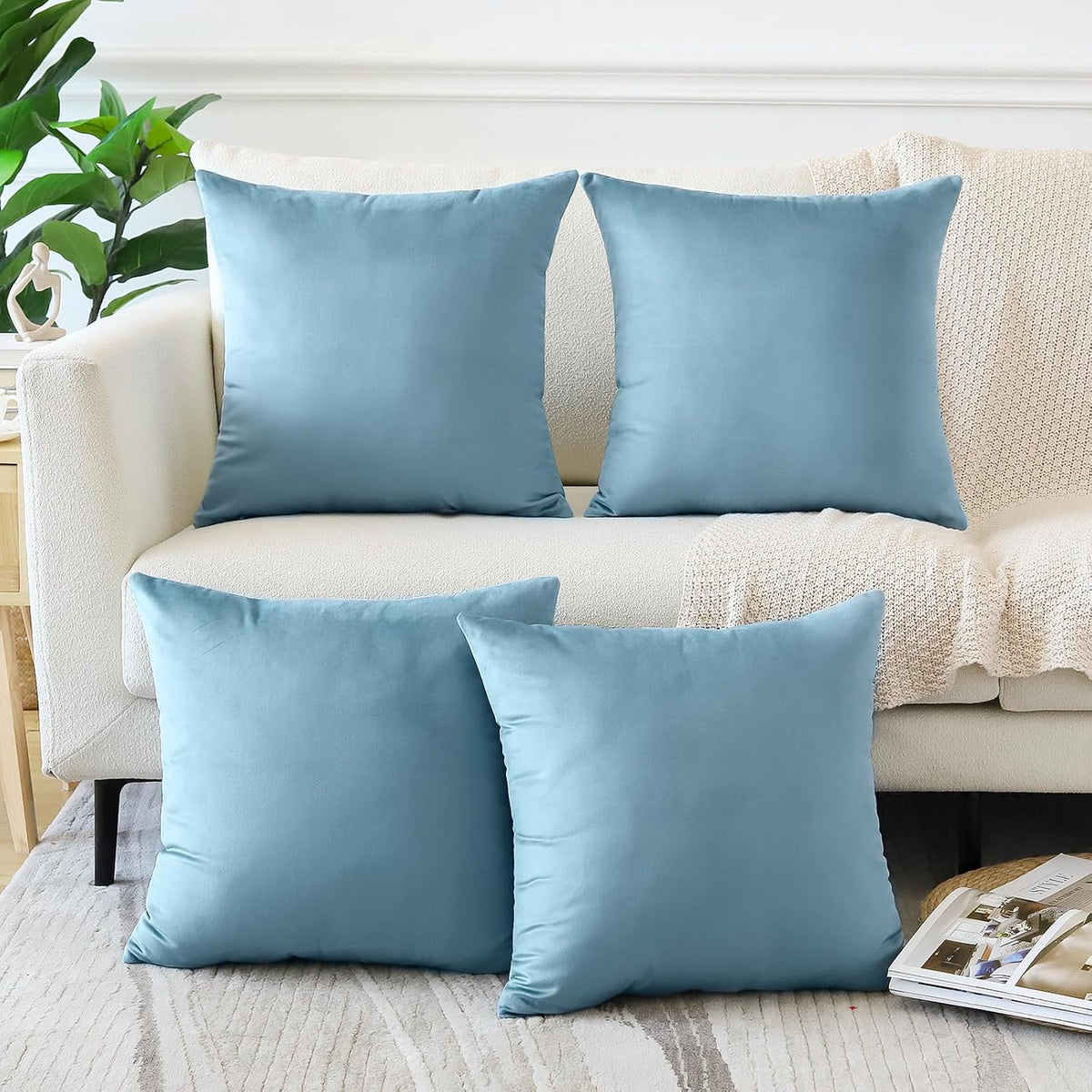 Two light-blue velvet square pillows on a cream sofa back with two matching pillows on the floor rug