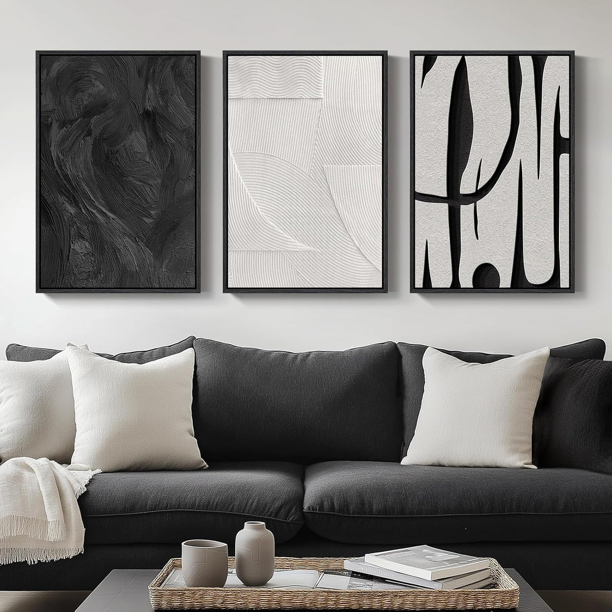 Three vertical framed abstract black-and-white prints hung above a dark gray sofa with light pillows and a coffee table.
