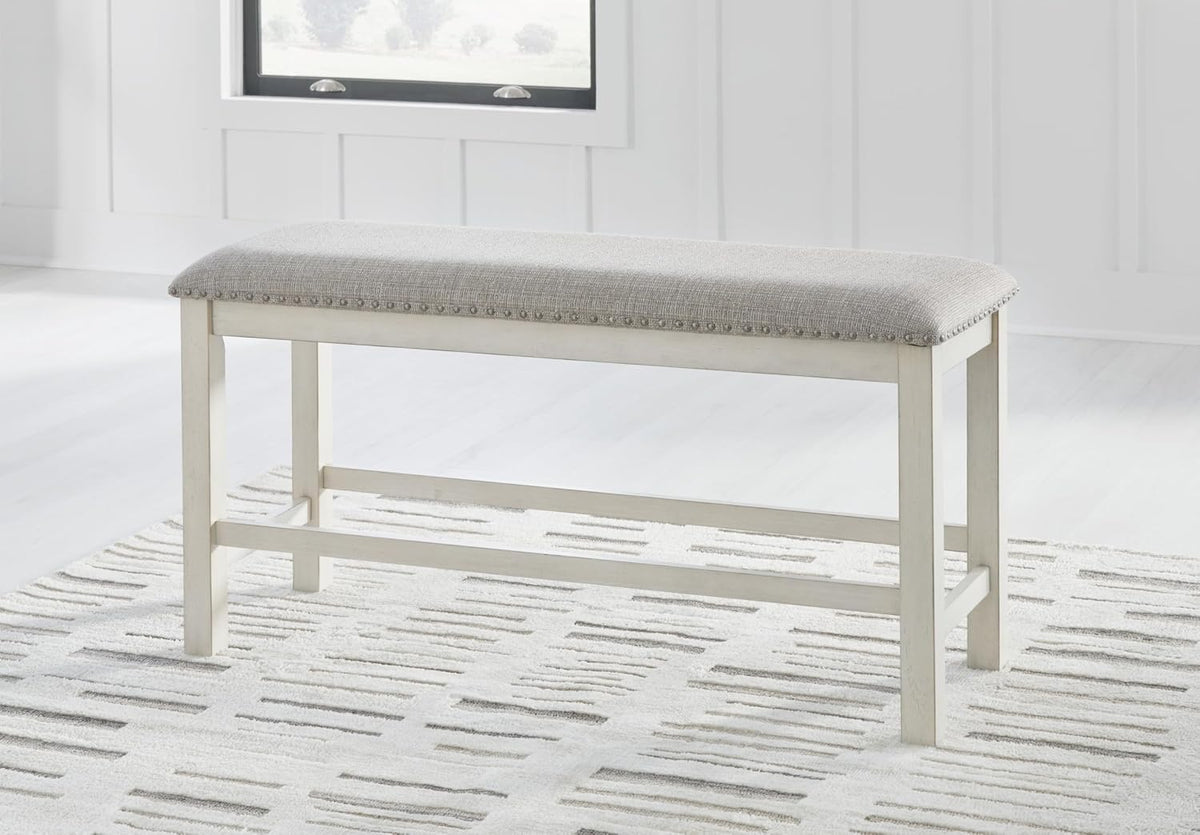 Light gray upholstered counter-height bench with antiqued white frame shown in a bright room on a patterned rug