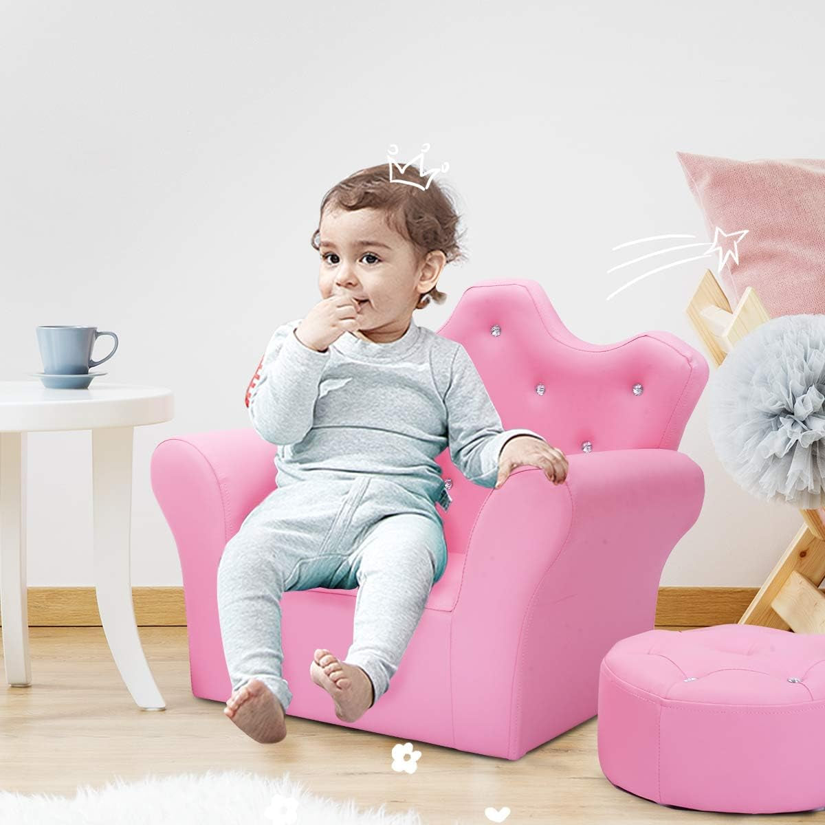 Toddler seated on a pink crown-back kids chair with matching round ottoman beside it in a bright playroom.