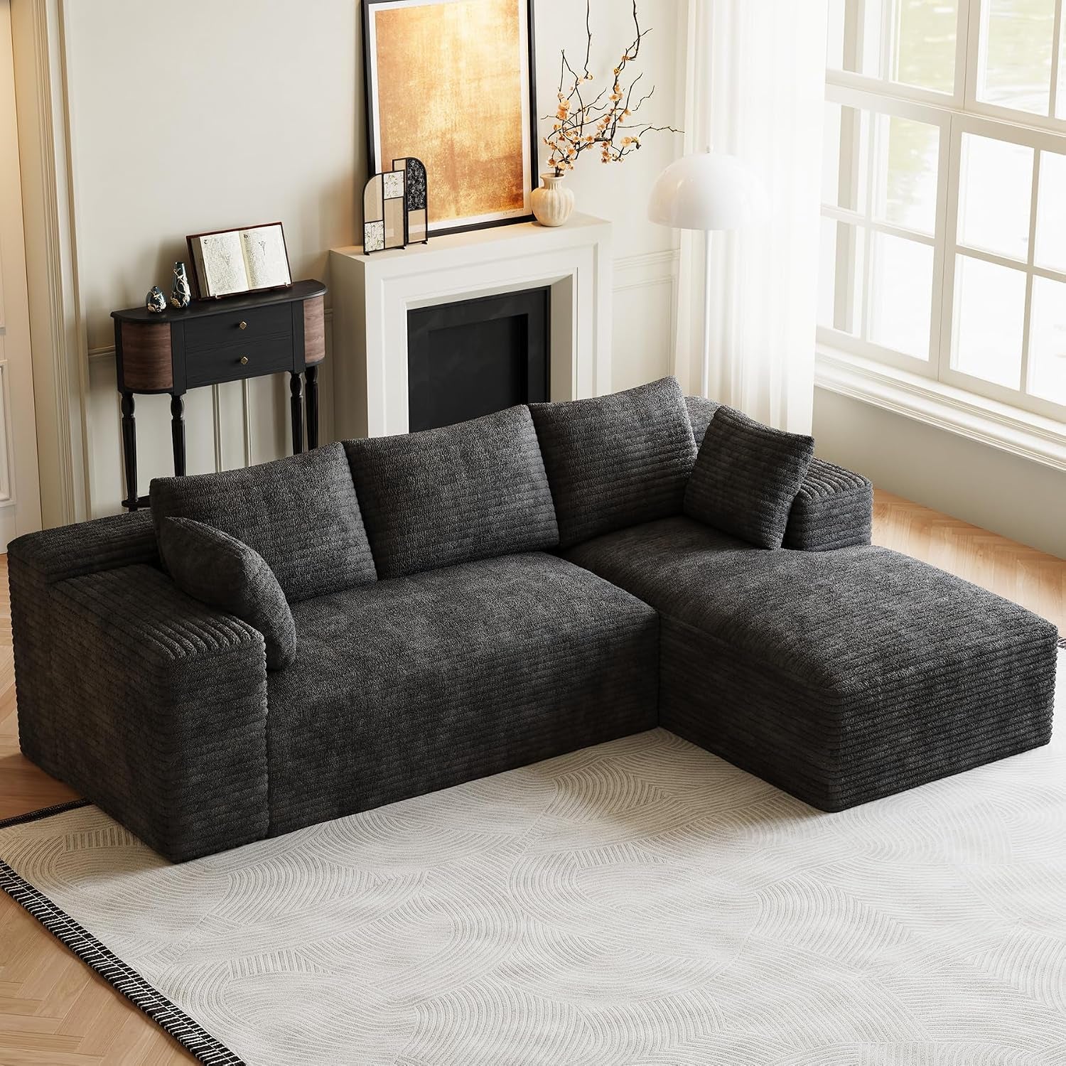 Charcoal L-shaped modular sofa with chaise placed by a large window on a light patterned rug.