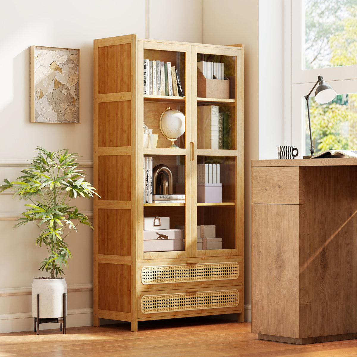 Bamboo bookcase with clear-panel doors closed, books and decor inside, beside a wooden desk.