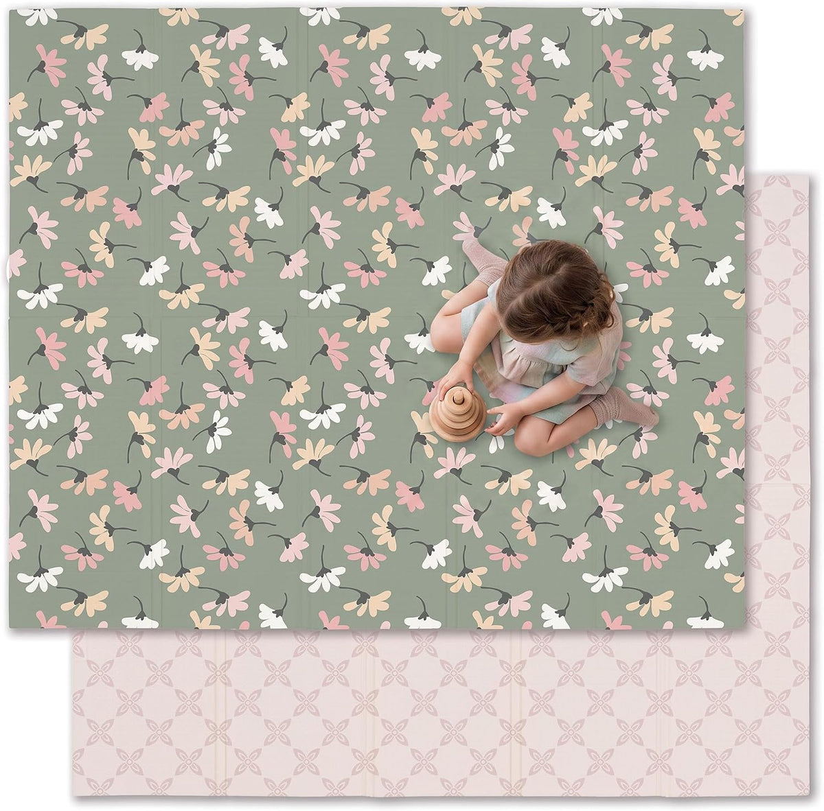 Top-down view of a child sitting on a green floral foldable play mat with the pale patterned reverse peeking out