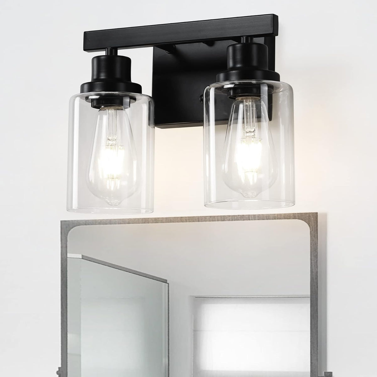 Close-up of a two-light bathroom vanity fixture with clear cylindrical glass shades and a black mount