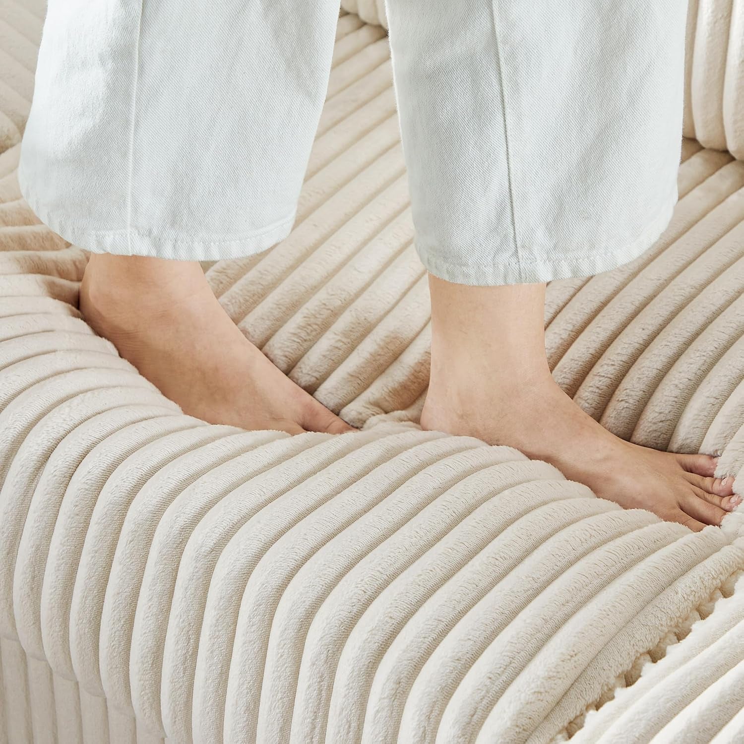 Close-up of bare feet pressing into the thick ribbed cream corduroy seat cushion.