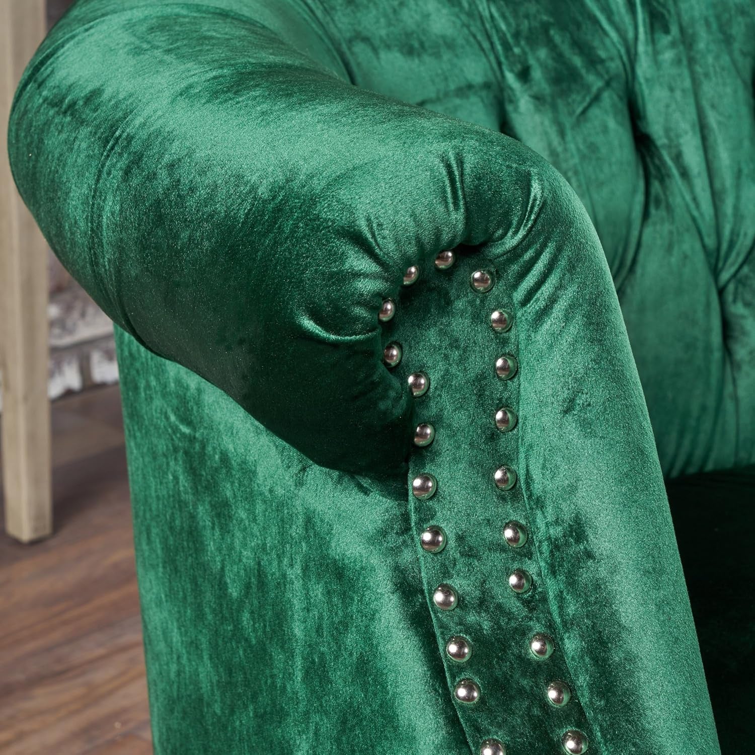 Close-up of scrolled arm and silver nailhead trim on emerald velvet upholstery