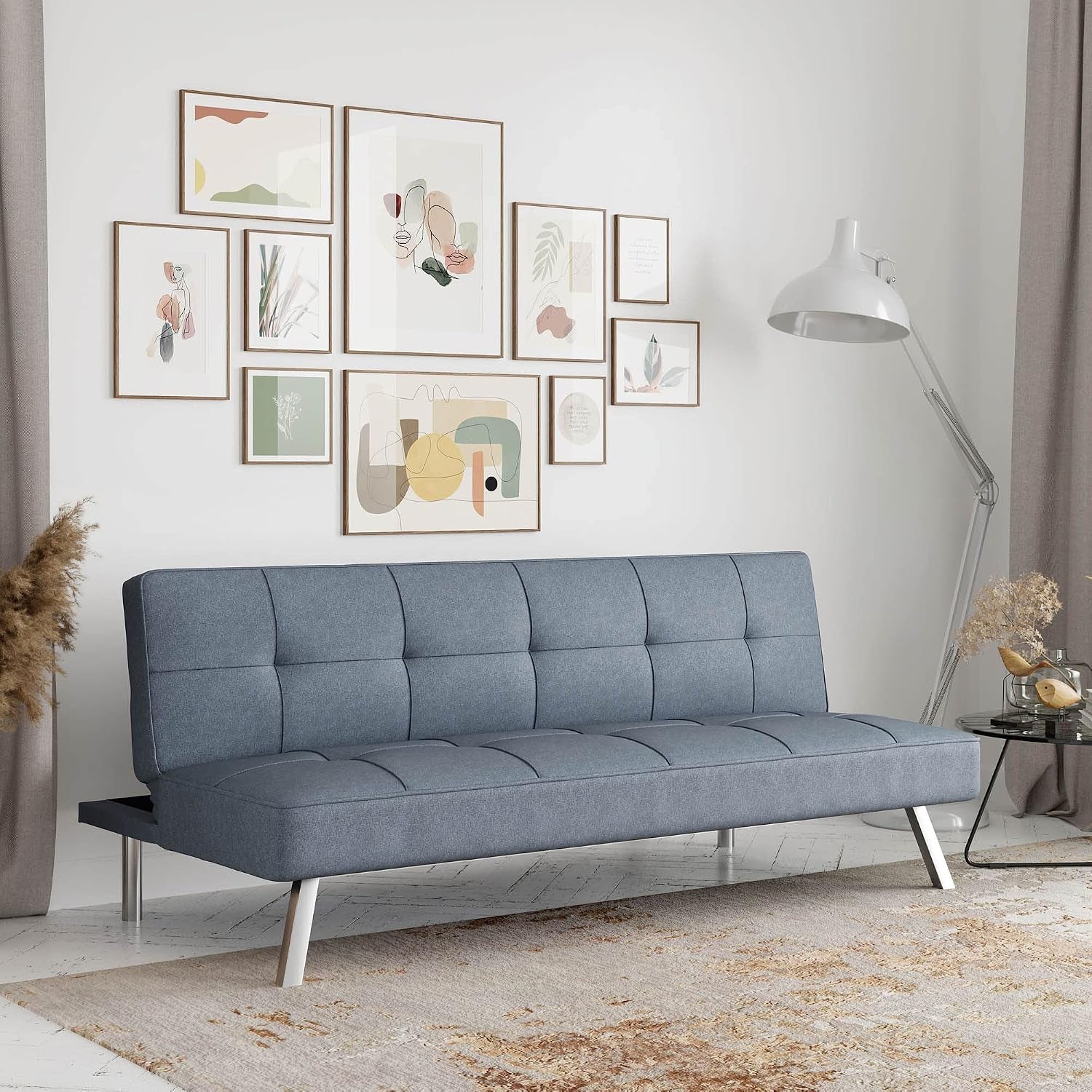 Tufted light blue-gray convertible futon sofa with chrome angled legs in a styled living room.