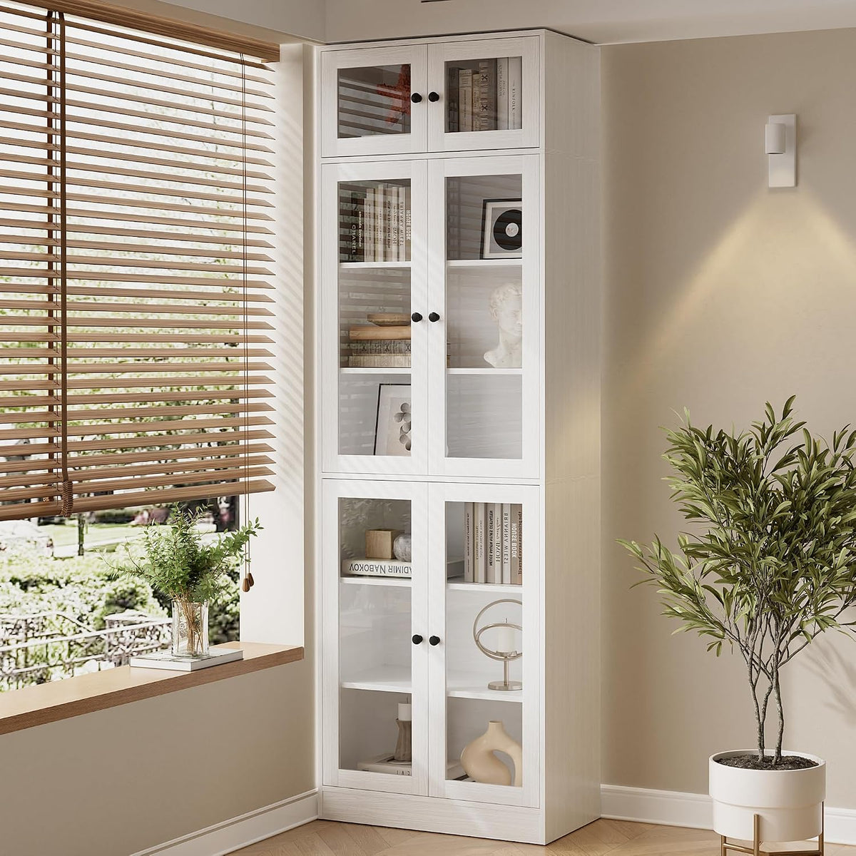 Tall white glass-door bookcase beside a window with wooden blinds