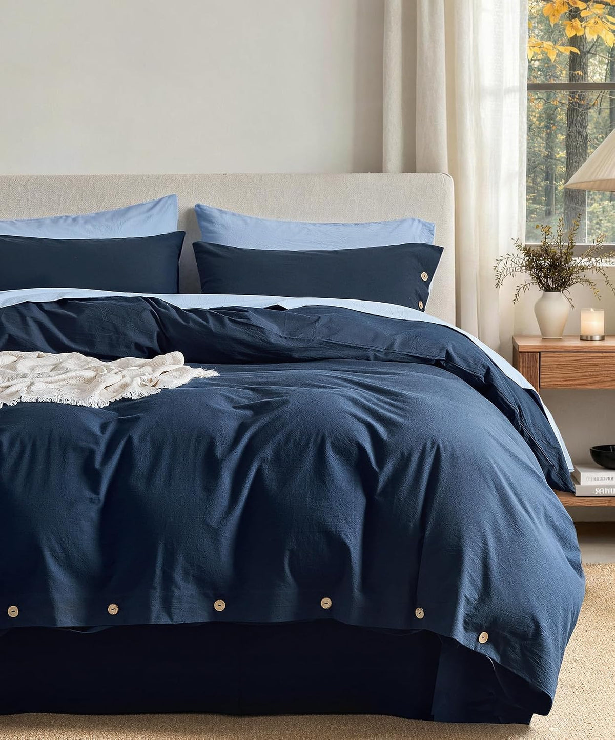 Bed dressed in navy duvet with light-blue reverse, beige headboard and nightstand at window.