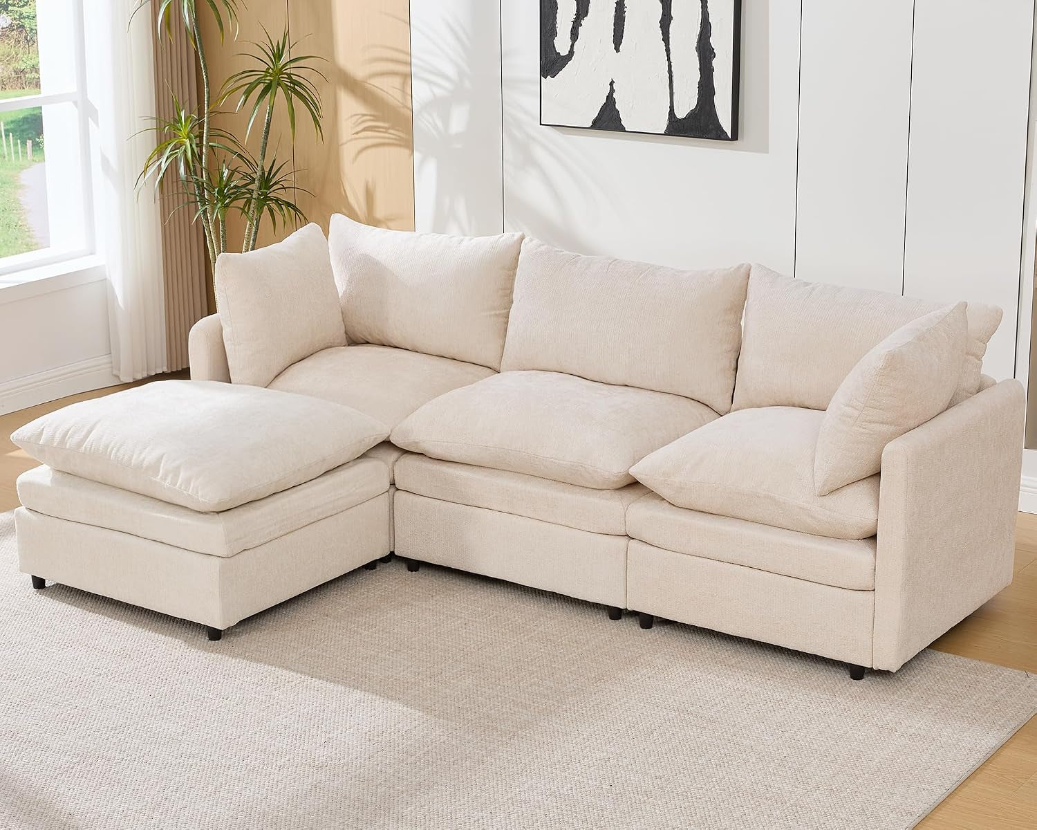 Cream three-seat modular sectional with a left-side ottoman in a bright living room.
