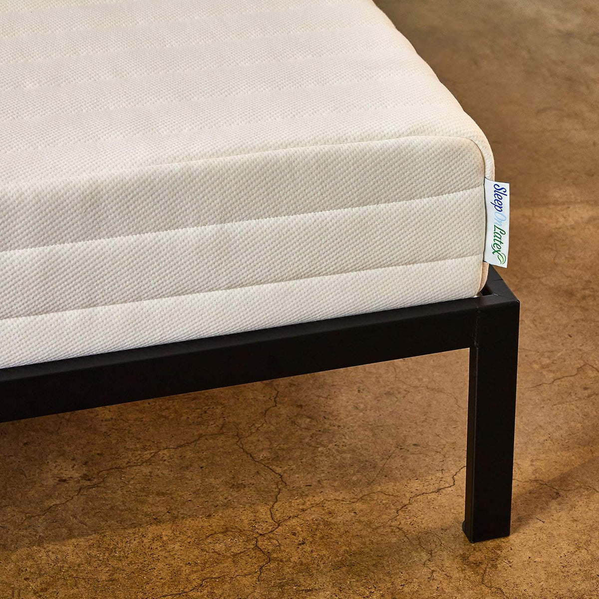 Cream-colored organic latex mattress corner on a black metal frame showing quilted cover texture.