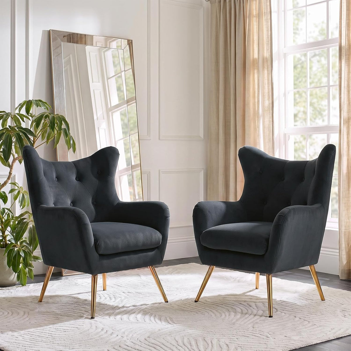 Two charcoal wingback chairs facing slightly inward with a large leaning mirror and plant
