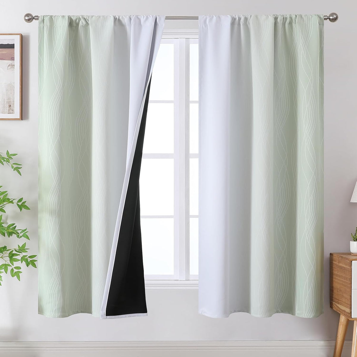 Window with two pale green ombre curtains on a rod, one panel pulled aside revealing white face and black blackout backing.
