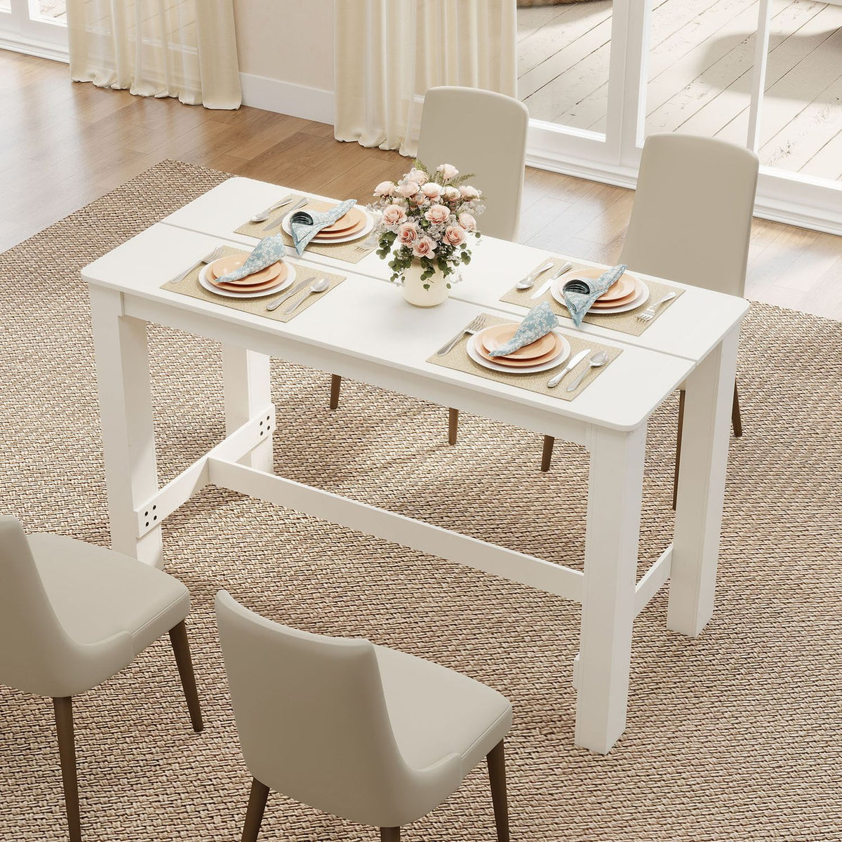 White rectangular table set with plates and flowers, viewed from above with chairs around it.