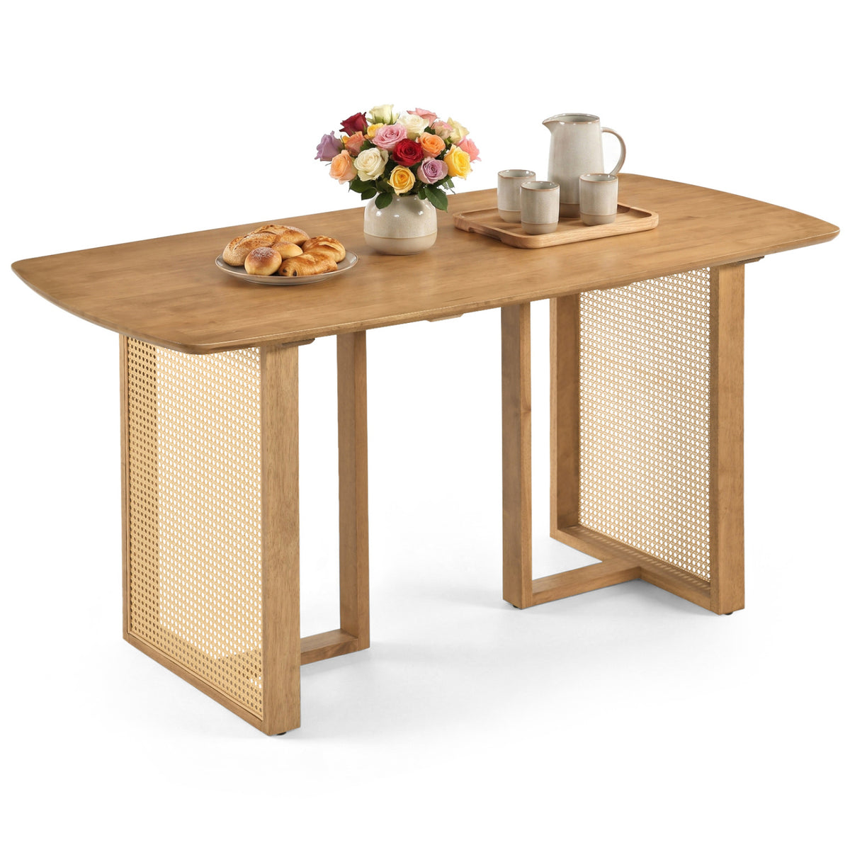 Woven-base dining table against white, set with flowers, pastries, cups, and a pitcher.