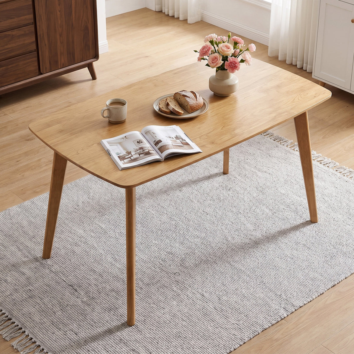 Natural wood dining table in a bright room, angled view with tableware