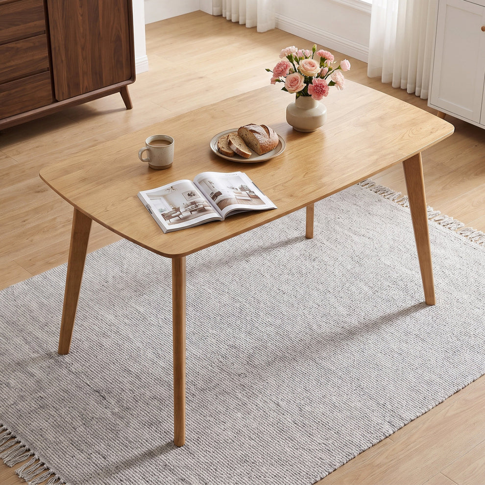 Natural wood dining table in a bright room, angled view with tableware