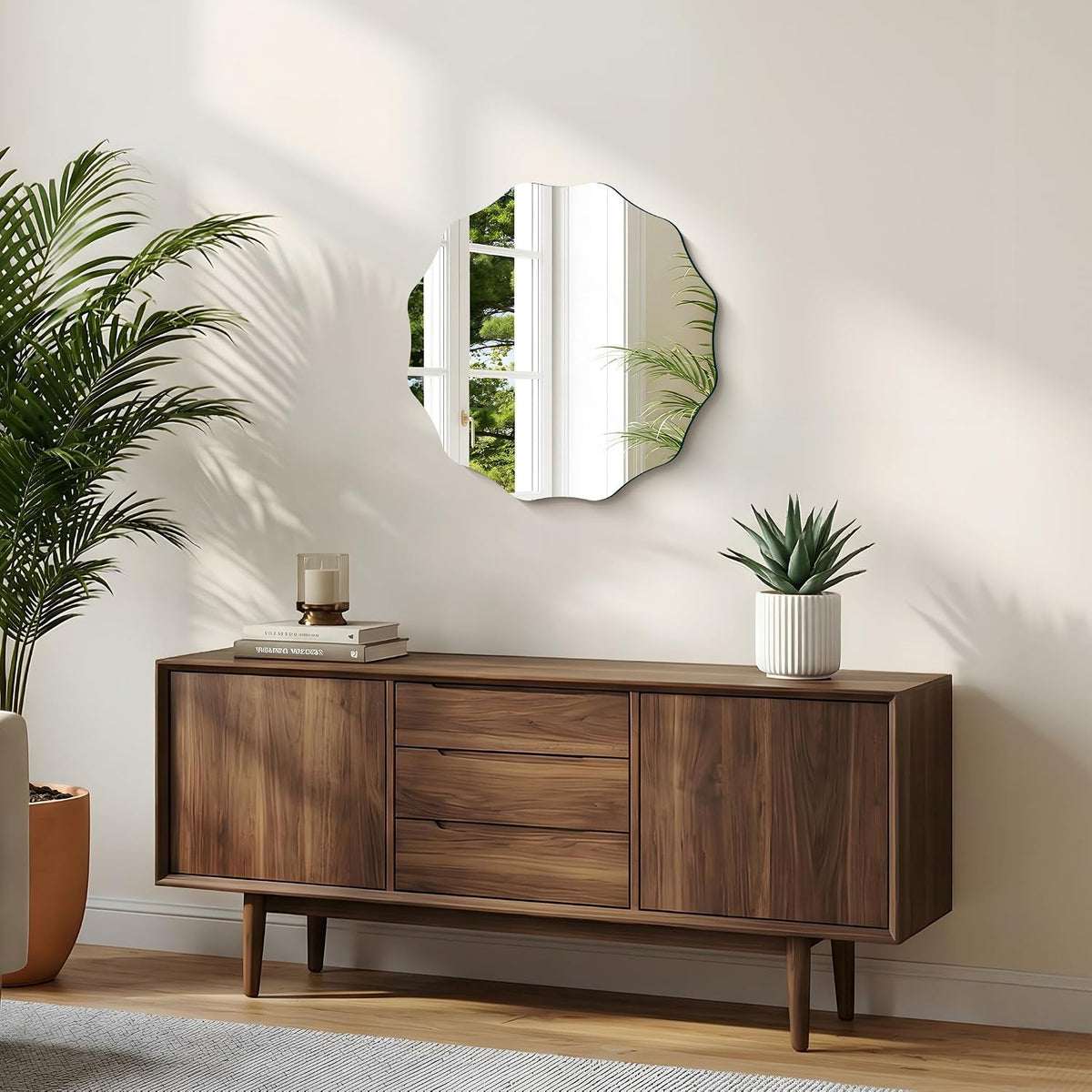 Scalloped round mirror hung above a mid-century wooden credenza with a potted succulent and stack of books.