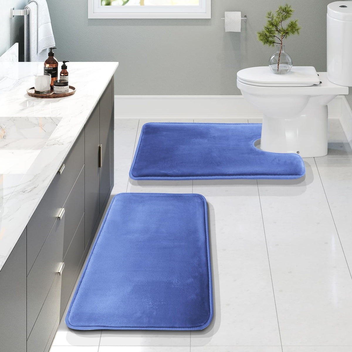 Overhead bathroom view showing three cobalt-blue bath rugs laid out along a vanity and at the toilet.