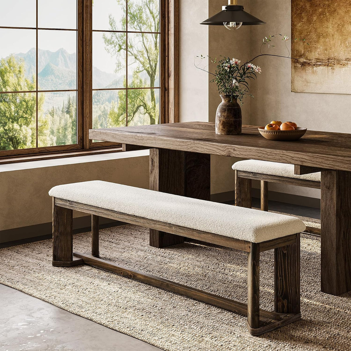 Bench shown in a dining setting tucked beside a rustic wood table on a woven rug by large paned windows.