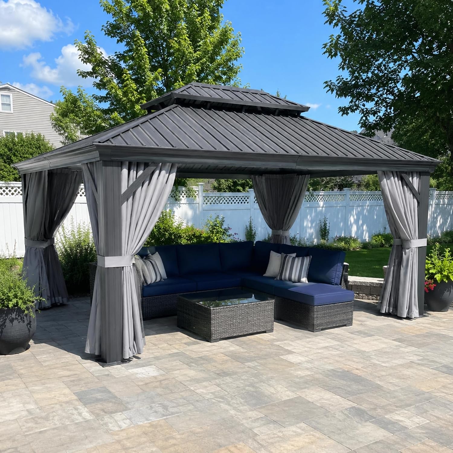 Gray hardtop gazebo with tied gray curtains over navy sectional, angled front view on stone patio