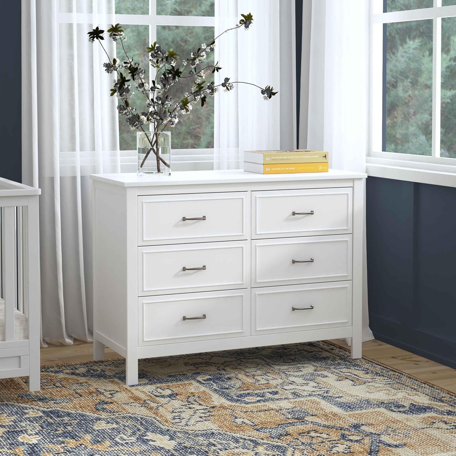 White six-drawer dresser beside a crib in a navy-walled nursery with patterned rug