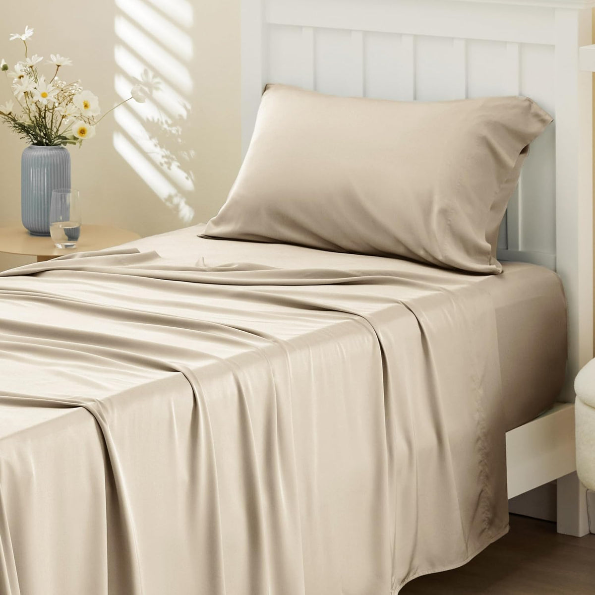 Angled front view of a bed with champagne-colored silky sheet and pillow, sunlight pattern on the wall and bedside table