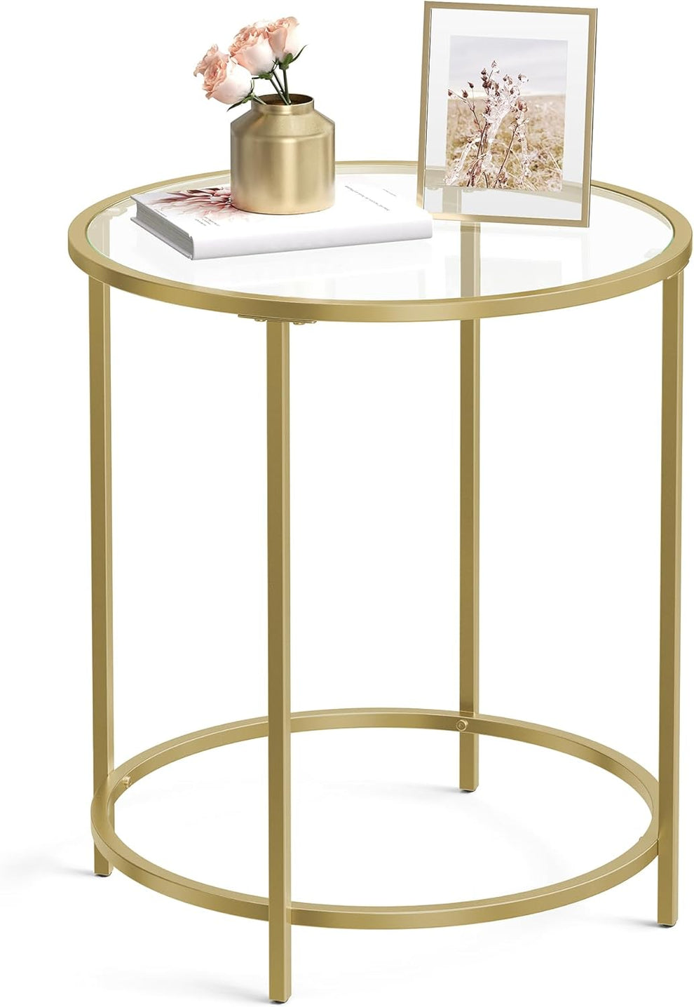 Round gold-colored steel side table with clear tempered glass top, angled front view with decor on top
