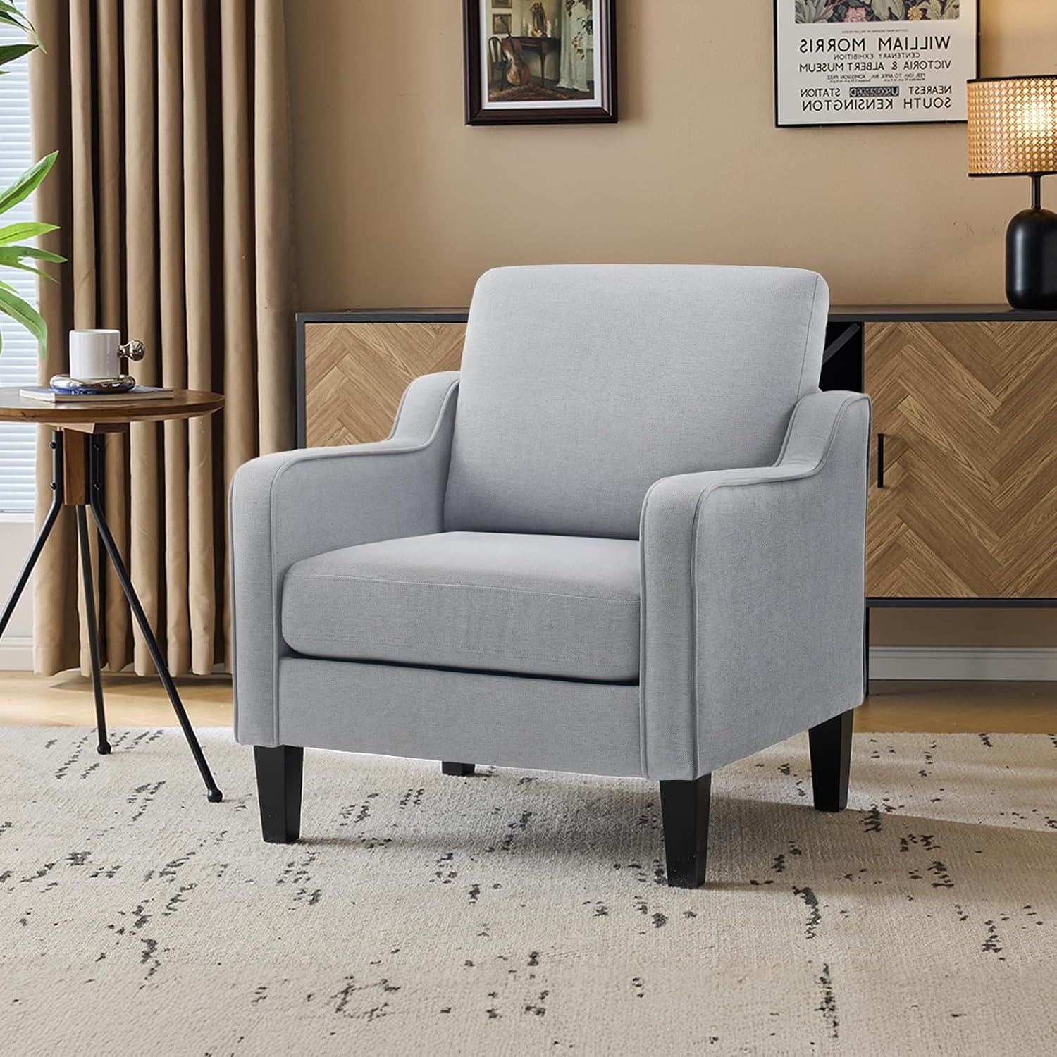 Light gray upholstered accent chair placed on a patterned rug beside a sideboard and window.