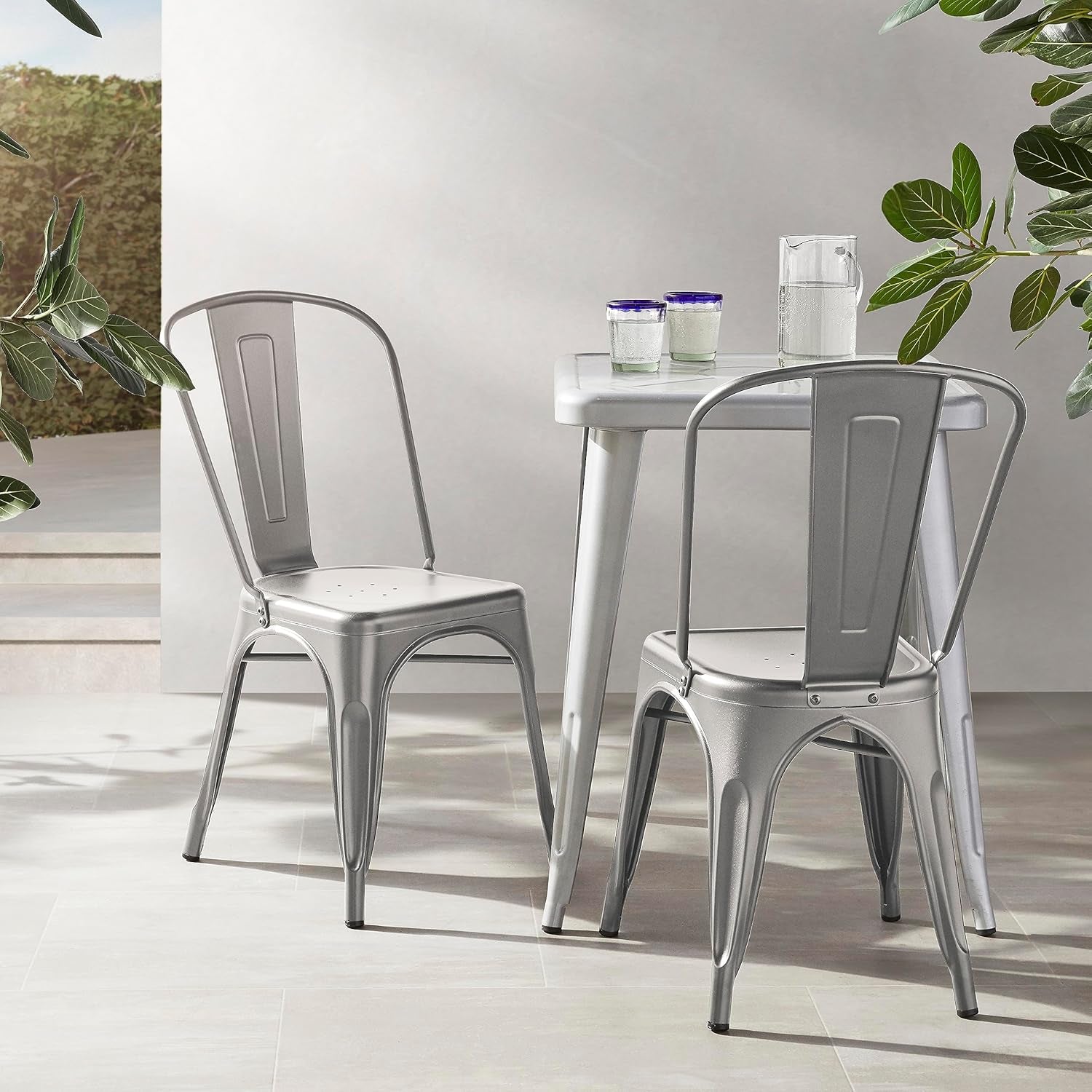 Two dark gray metal dining chairs beside a small white table in a bright indoor setting