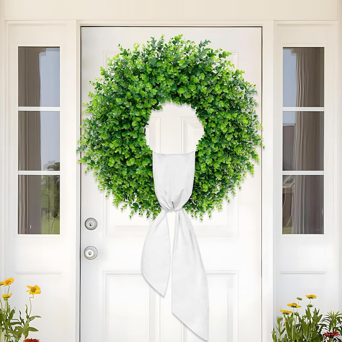 Single large boxwood wreath centered on a white front door, tied with a long white sash and flanked by sidelights.