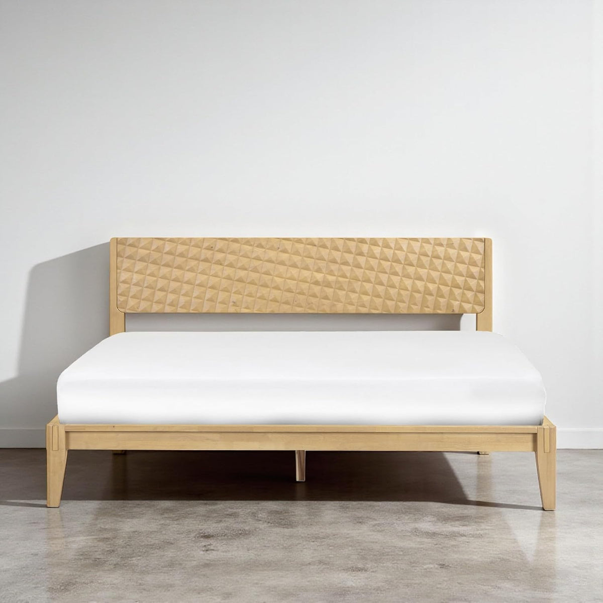 Centered front shot of the bed in light wood with sunlight casting a shadow on the wall left of the headboard.