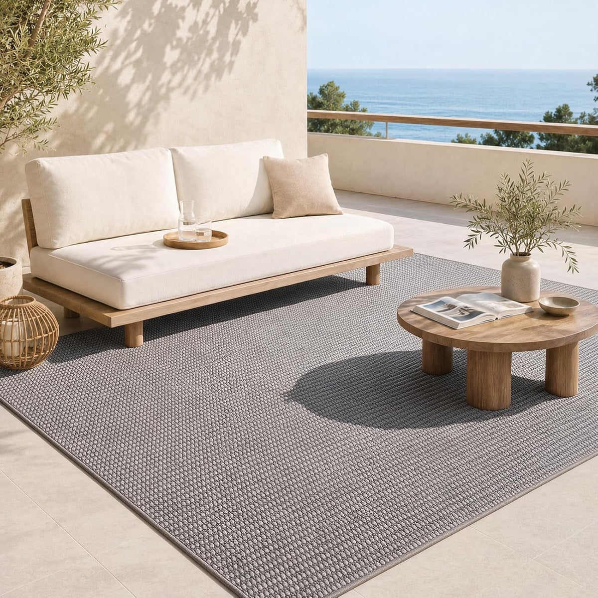 Grey jute-style rug on a sunlit terrace beneath a low wooden sofa and round coffee table with ocean view.