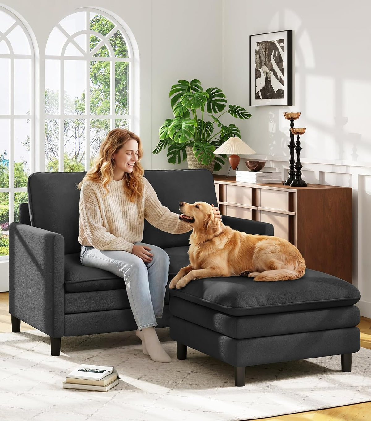 Charcoal loveseat paired with a matching ottoman, woman petting a golden retriever on the ottoman.