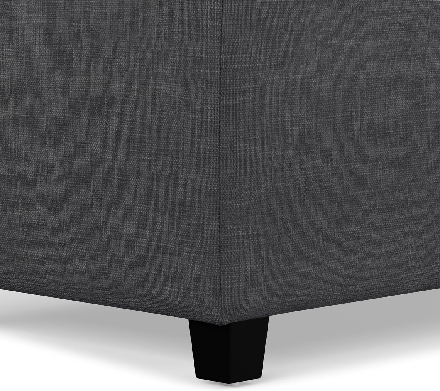 Close-up of ottoman corner showing slate-gray linen-look fabric and a short black tapered leg.