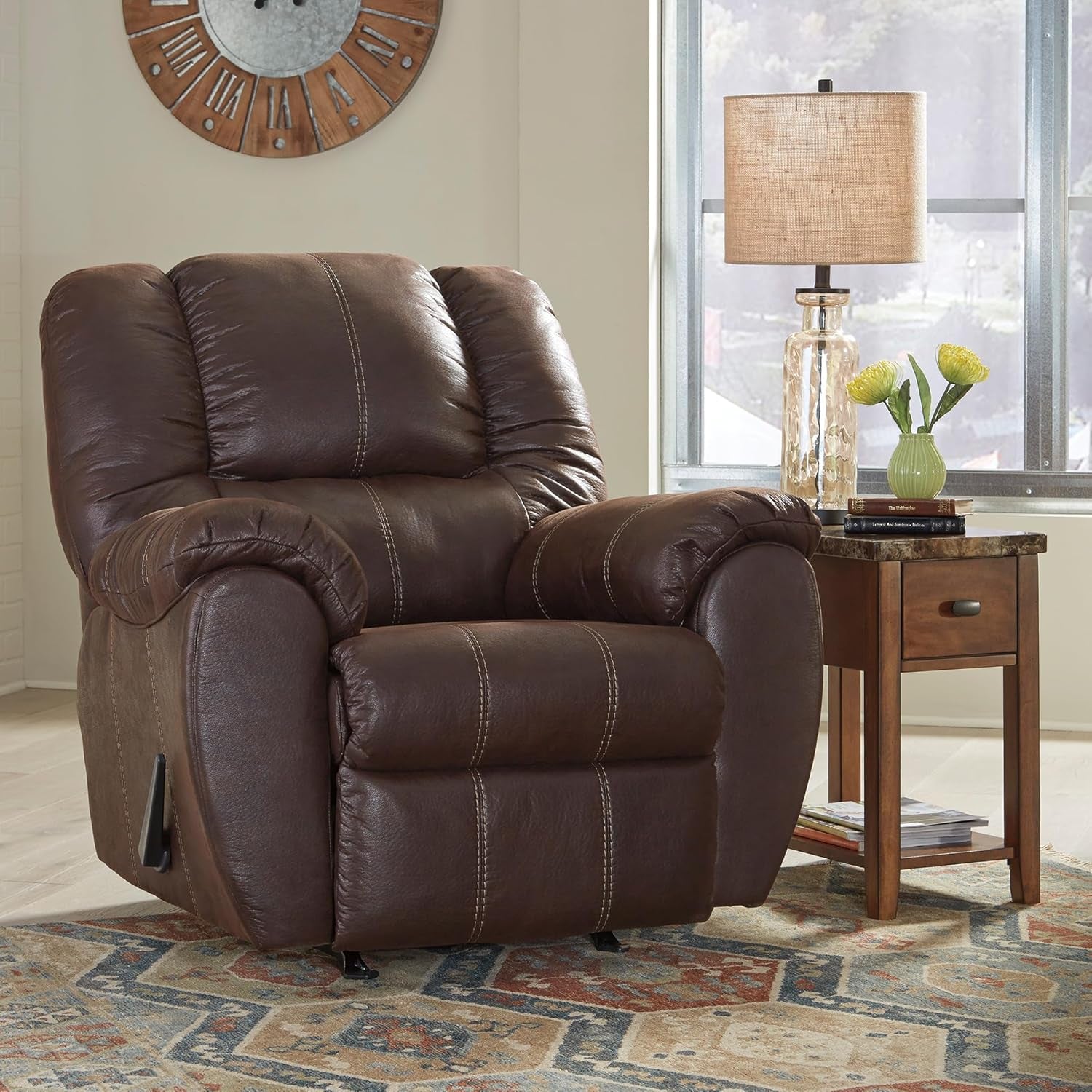 Brown faux leather recliner in a living room setting beside a wooden side table and lamp