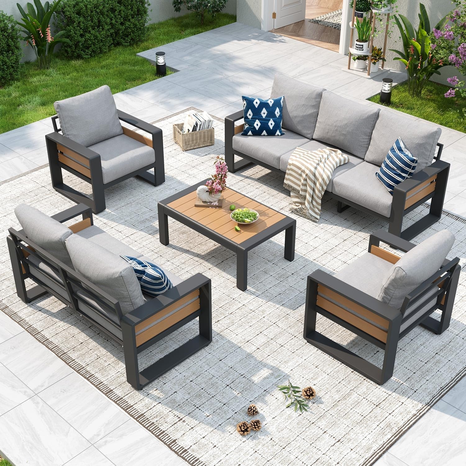 Top-down shot of light-gray cushioned patio sofa and chairs with a low wood-top coffee table and decorative accents.