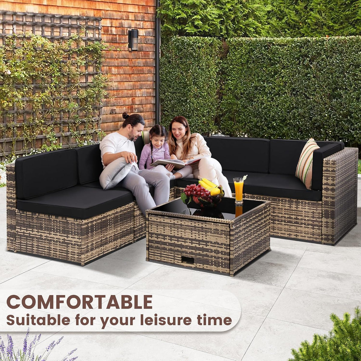 Corner view of rattan sectional with black cushions and tempered glass table, family seated to show scale