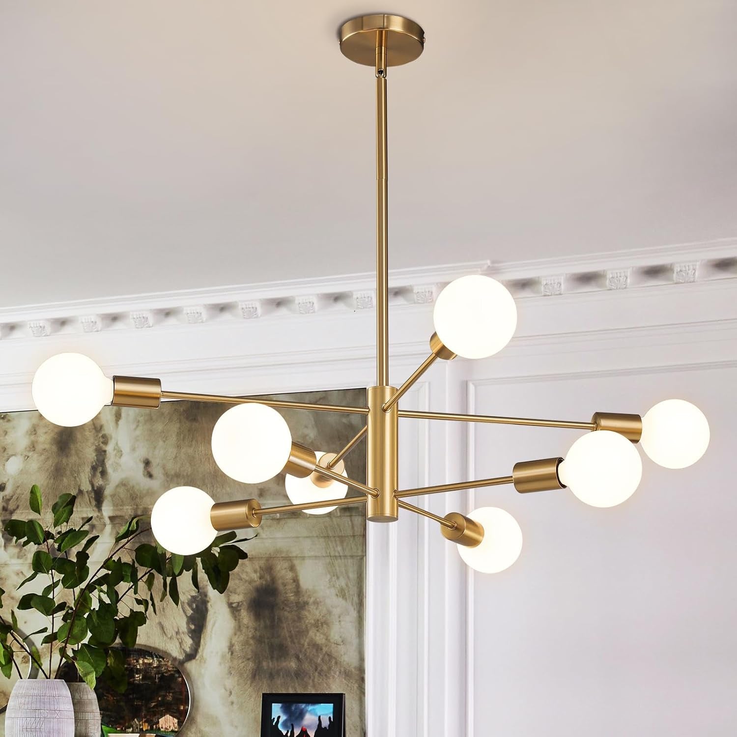 Gold-finished sputnik chandelier with glowing globe bulbs hanging above a framed wall and plants.