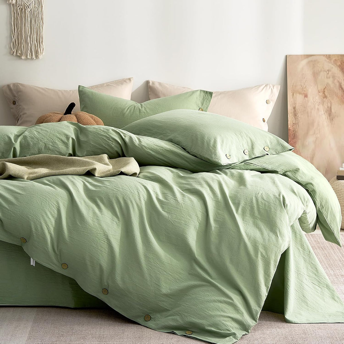 Casually styled bed with light mint green duvet and layered pillows, decorative throw and wall art at right.