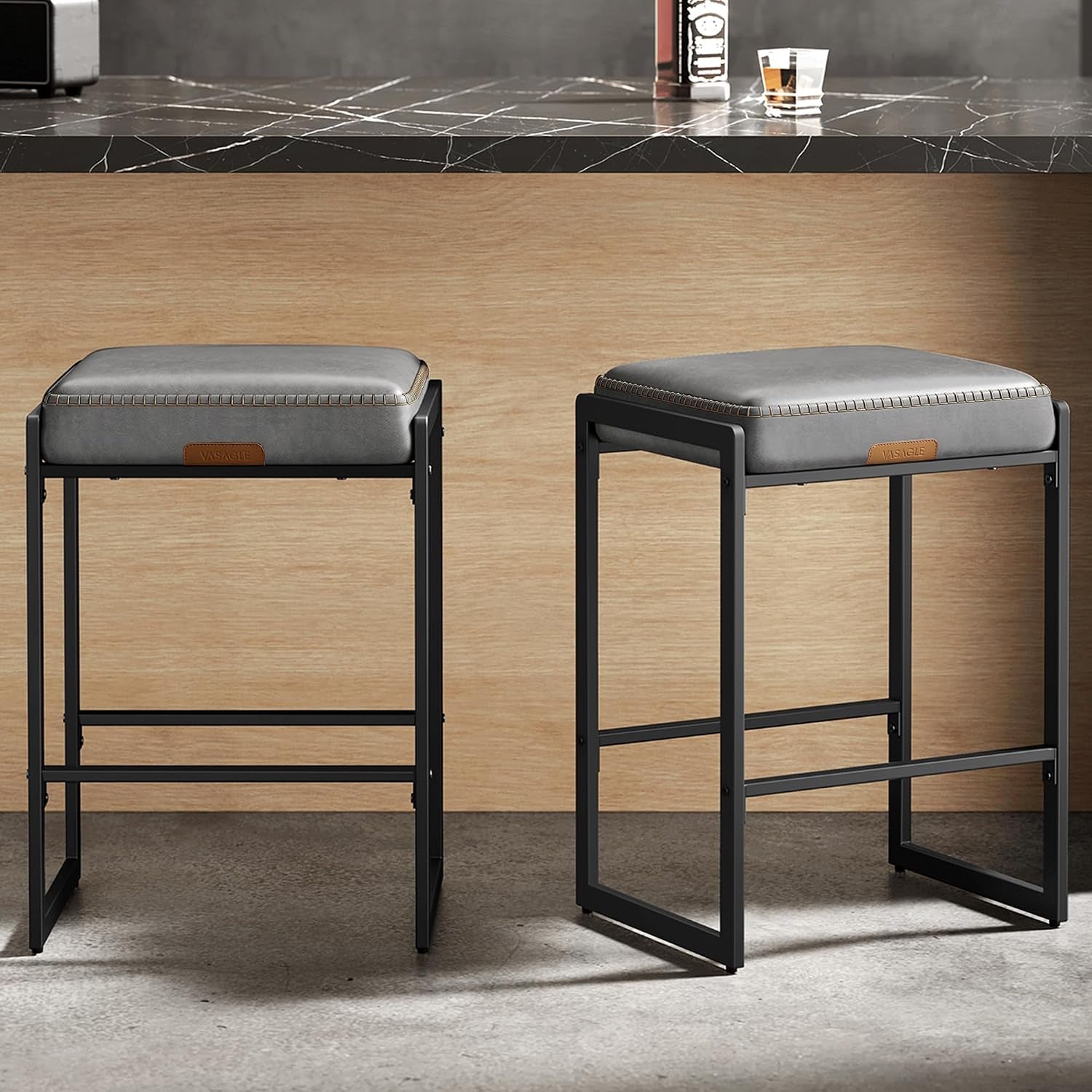 Pair of gray-cushioned counter stools shown side-by-side against wood paneling beneath a dark veined countertop