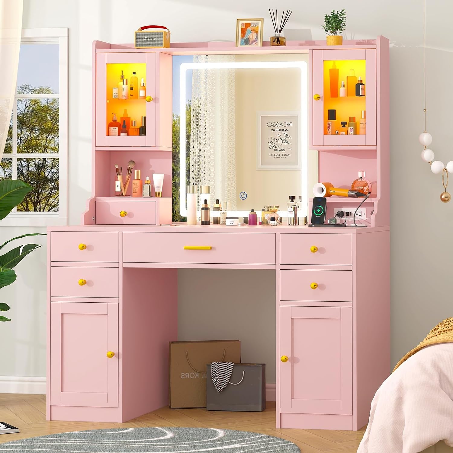 Pink vanity set in a bedroom scene with mirror lit and shopping bags stored under the desk.