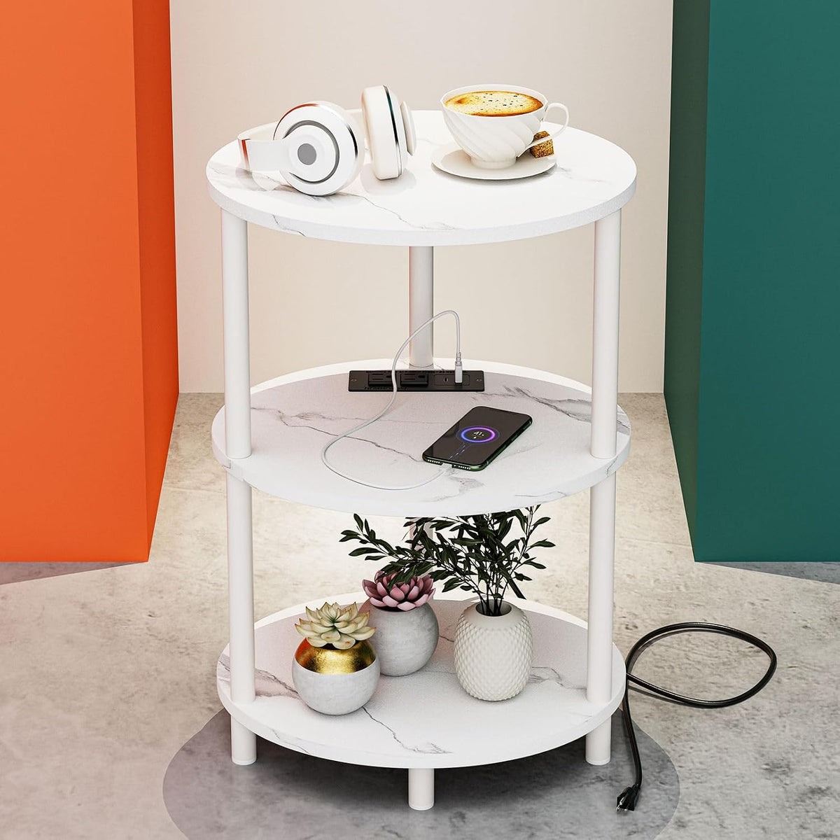 Three-tier round white marble-pattern end table staged with headphones, a cup, a phone, and small potted plants.
