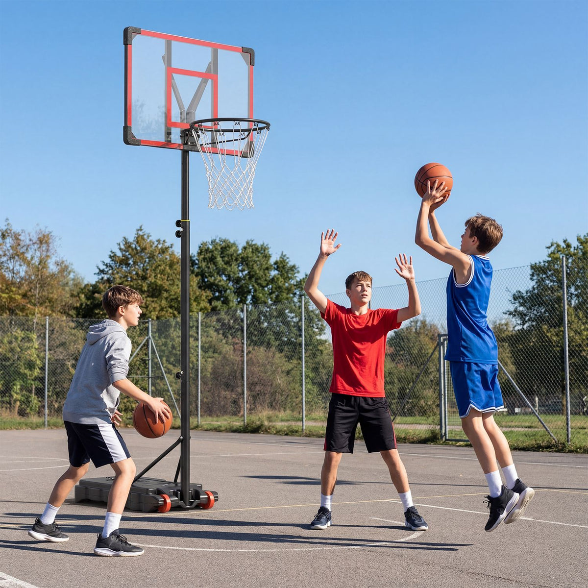 Three boys play basketball around a freestanding hoop on an outdoor court.
