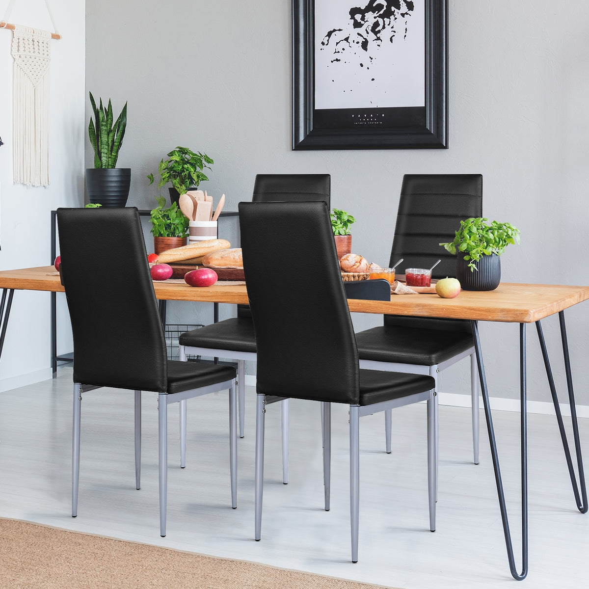 Four black dining chairs arranged around a wooden table set with food and plants.